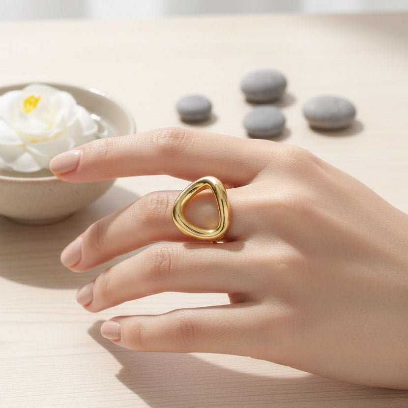 Hand wearing a gold ring with a bowl of white flowers and gray stones in the background