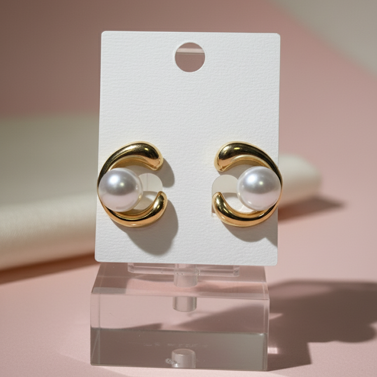 Gold earrings with pearls on a white card against a pink background