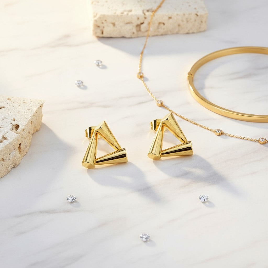 Gold triangle earrings on a light background with other jewelry items.