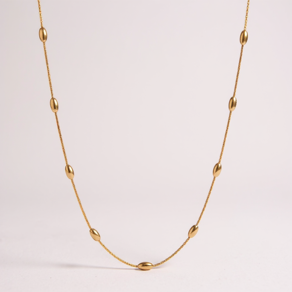 Gold necklace with small beads on a light pink background