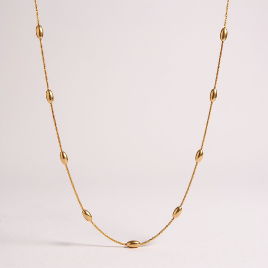 Gold necklace with small beads on a light pink background