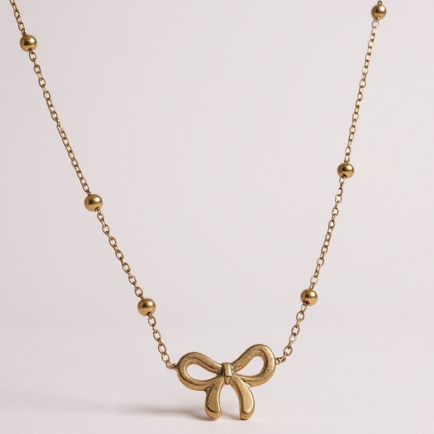 Gold bow-shaped necklace on a light pink background