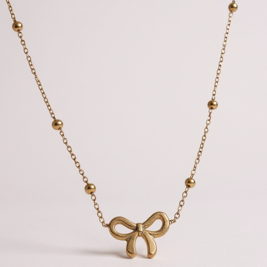 Gold bow-shaped necklace on a light pink background