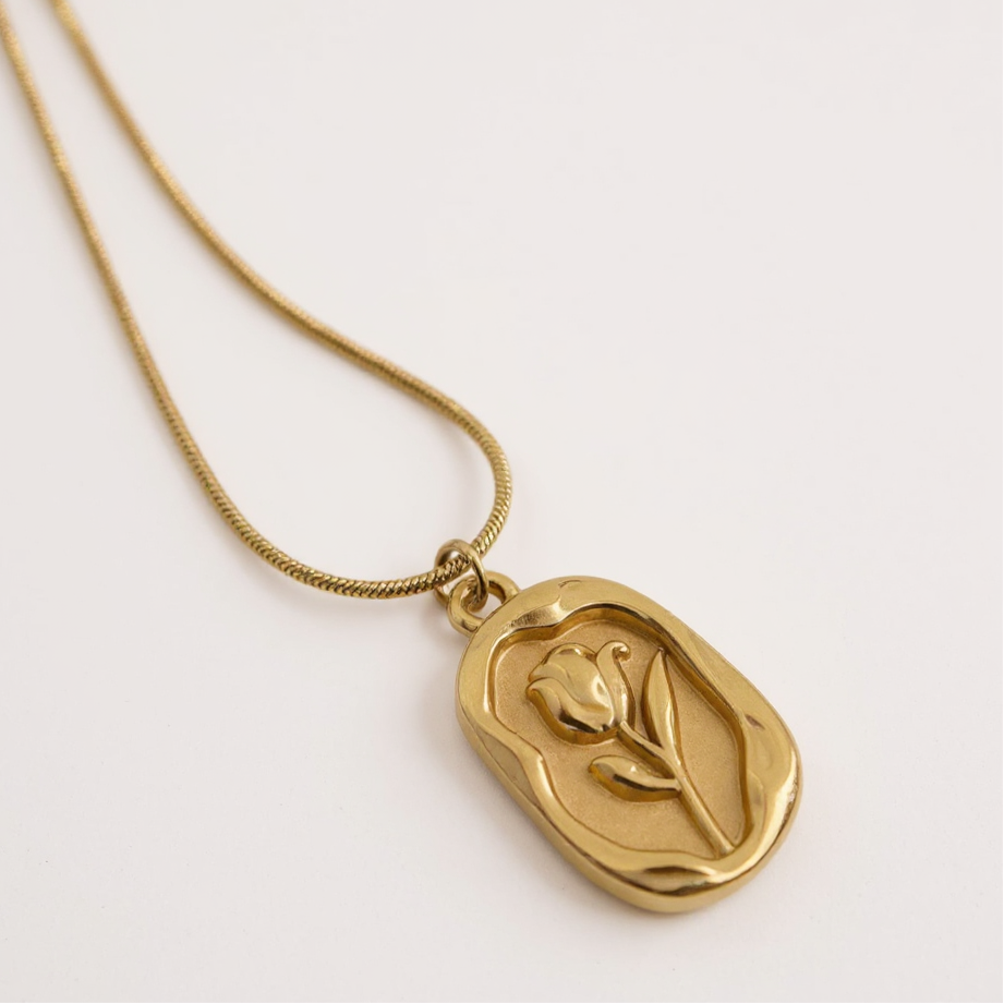 Gold necklace with a tulip-shaped pendant on a light gray background